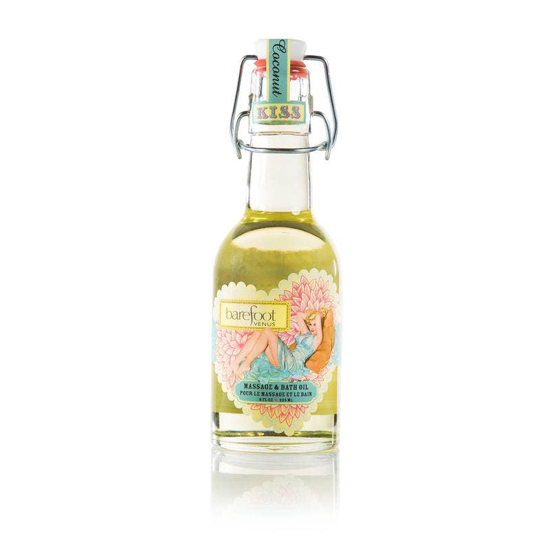 A bottle of Barefoot Venus Coconut Kiss Body + Bath + Massage Oil in Coconut Kiss flavor, made with natural oils. The clear bottle features a colorful label depicting a relaxed woman and is secured with a metal clasp. The pale yellow multi-purpose oil inside promises a delightful experience.