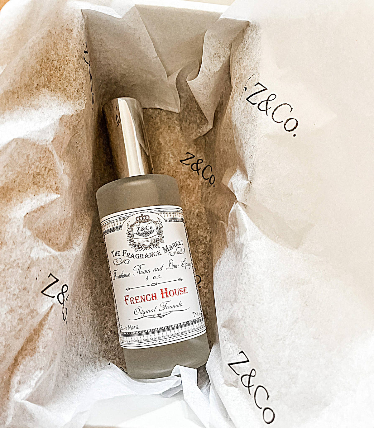 A bottle of Z&Co. Salt Farmhouse Room/Linen Spray rests on white Z&Co.-printed tissue paper inside a box, featuring a silver cap and a vintage-style label. Handcrafted in Texas by Z&Co.