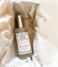 A bottle of Z&Co. Salt Farmhouse Room/Linen Spray rests on white Z&Co.-printed tissue paper inside a box, featuring a silver cap and a vintage-style label. Handcrafted in Texas by Z&Co.