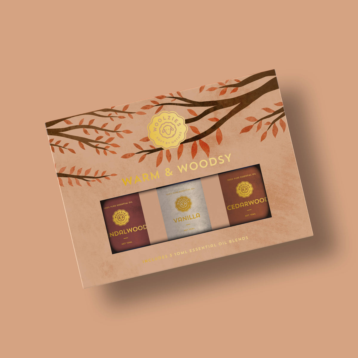 The Woolzies Warm & Woodsy Collection boxed set features vanilla, sandalwood, and cedarwood essential oils. The brown packaging shows leaf illustrations and displays the Woolzies brand logo.