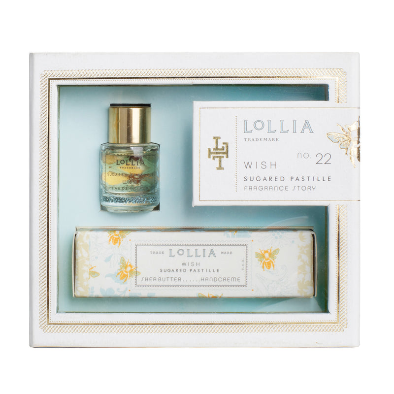 A delightful Margot Elena Lollia Wish Fragrance Story Gift Set in light blue and white, adorned with gold decorative accents, includes a small bottle of Lollia Wish Eau de Parfum and a Shea Butter Handcreme. The set is elegantly displayed in a white box with a clear front cover.