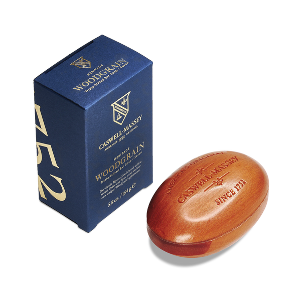 A blue box labeled "Caswell-Massey Sandalwood Woodgrain Bar Soap" stands beside an oval, woodgrain-textured triple-milled soap engraved with "Caswell-Massey Since 1752.