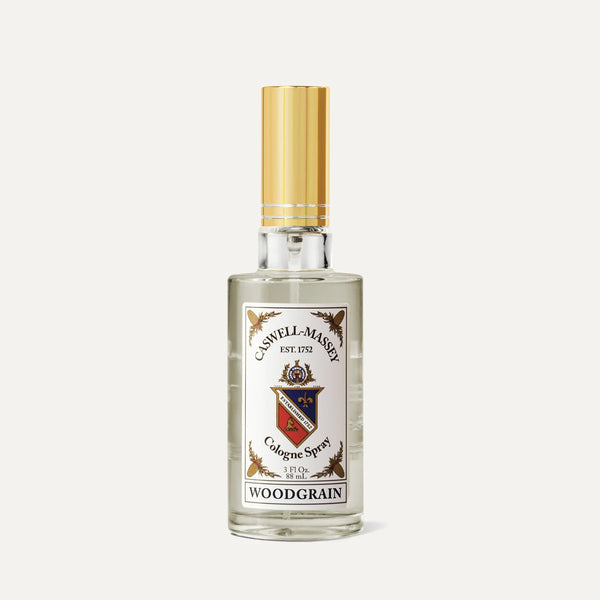 A clear glass spray bottle of Caswell-Massey Woodgrain Sandalwood Cologne with a gold cap and detailed label on a plain light background—ideal for fans of classic woody scents.