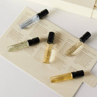 Five small Caswell-Massey eau de parfum vials are arranged on a cream-colored card with printed descriptions, set atop a white surface with matching packaging—a perfect Caswell-Massey Fragrance Discovery Collection for men.