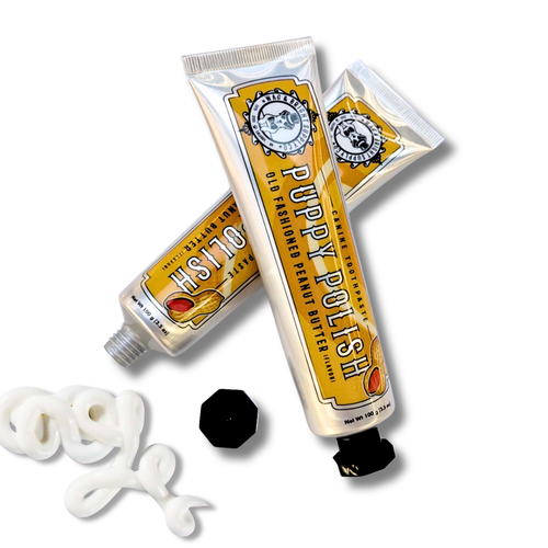 Two metallic tubes of Wag & Bright Supply Co. Puppy Polish Toothpaste - Old Fashioned Peanut Butter with dog logos are shown, one open with cream swirled out; natural dog toothpaste with black caps nearby.