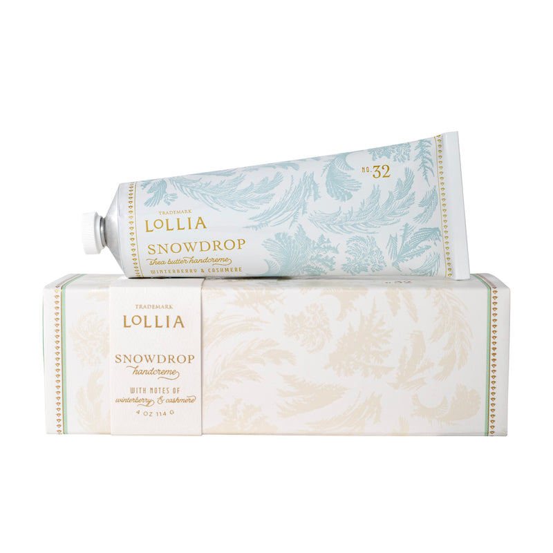 A tube of Margot Elena Lollia Snowdrop Handcreme sits atop its matching decorative box, both adorned with light blue and gold floral designs and elegant text.