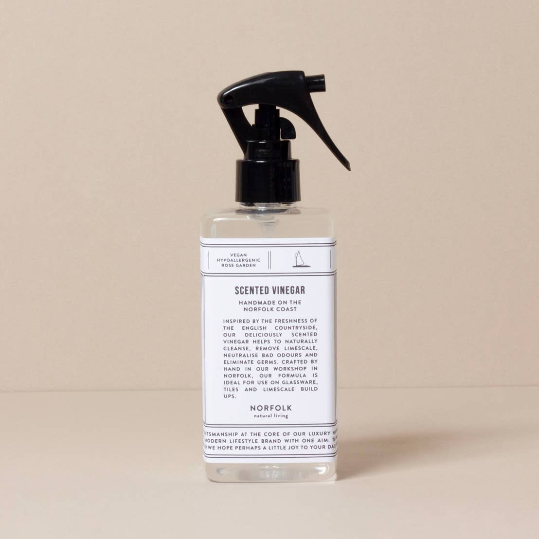 A clear spray bottle of Norfolk Natural Living Rose Garden Scented Vinegar sits on a neutral surface. This vegan, eco-friendly cleaner by Norfolk Natural Living is ideal for surfaces and glass, leaving a fresh rose garden fragrance.