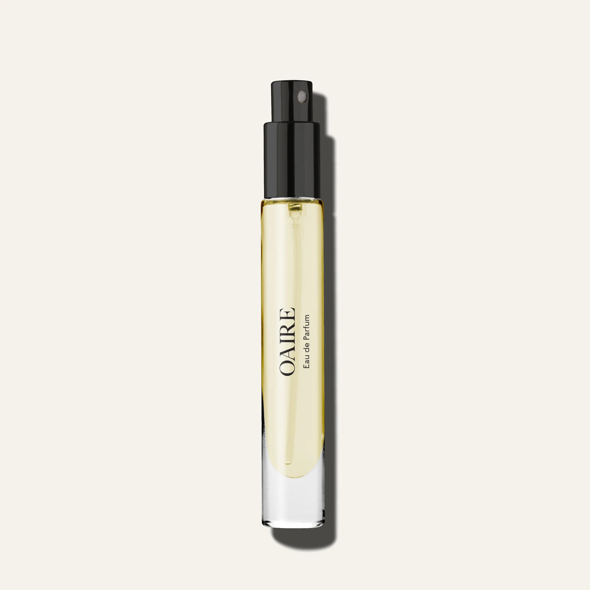 A clear glass Caswell~Massey Oaire Eau de Parfum bottle with light yellow liquid, black spray nozzle, and "OAIRE" written vertically is set against an off-white background, showcasing this aromatic fougere fragrance from Caswell Massey.