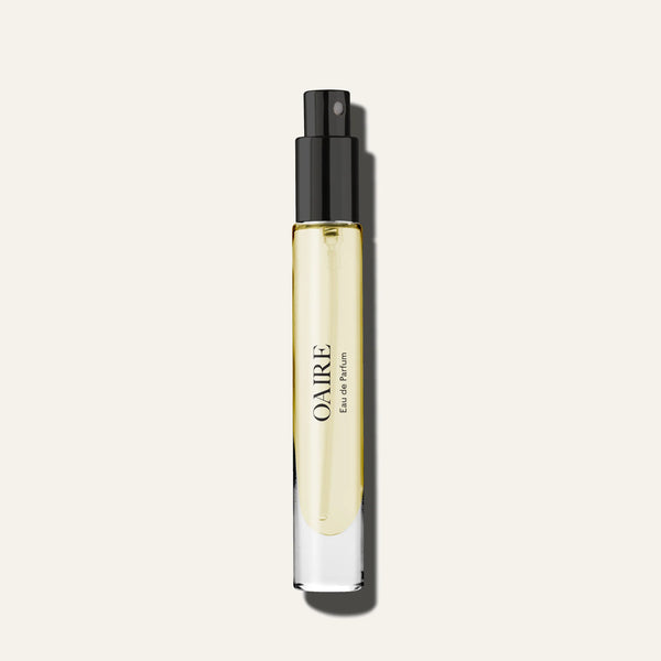 A clear glass bottle filled with yellow Caswell~Massey Oaire Eau de Parfum features a black spray nozzle and hints of Citrus Zest, set against a plain off-white background.