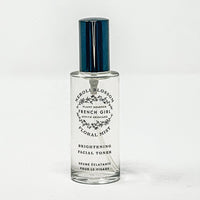 A clear glass bottle of FRENCH GIRL Organic Floral Face Mist & Toner - Neroli Blossom, a hydrating organic toner with a silver cap, stands upright on a white surface.