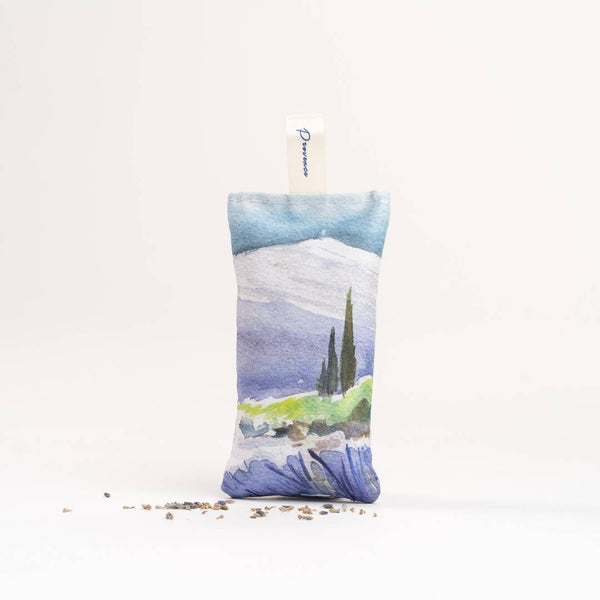 The L'AUGUSTE Provence - Organic French Lavender Sachet is small and rectangular, featuring a watercolor design of a Provencal landscape with mountains, trees, and flowers on a white background. It's filled with organic French lavender for stress relief, with dried pieces at the base and an attached tag.