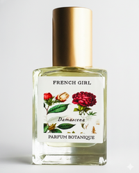 A clear glass perfume bottle with a gold cap, labeled "FRENCH GIRL Damascena Rose Organic Vegan Natural Aromatherapy Perfume," features floral artwork and contains an alcohol-free fragrance made from natural essential oils.