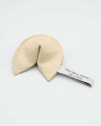 The MODERNBEAST Kitty Fortune Cookie Organic Catnip Cat Toy is a beige eco felt toy shaped like a fortune cookie, featuring a white fabric slip reading “YOU WILL HAVE TO LIVES”—a playful addition for your cat.