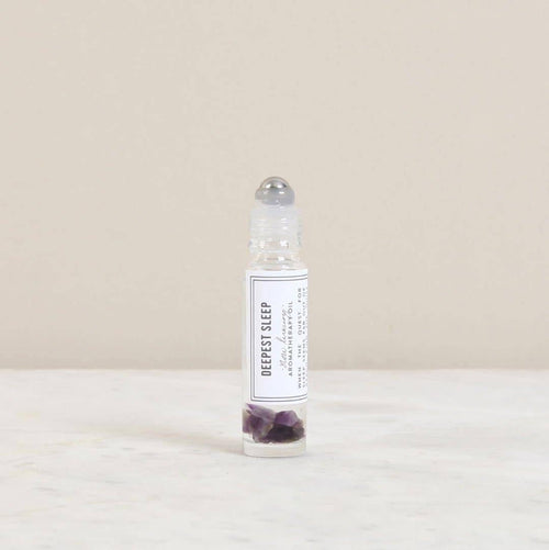 A 10ml Norfolk Natural Living Deepest Sleep Pulse Point Oil stands on a light marble surface with amethyst gemstones inside, supporting calm and restful sleep.