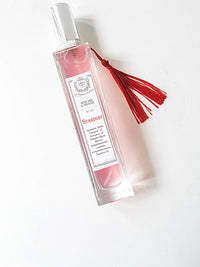 A rectangular glass bottle of Z&Co. Farmhouse Collection Body Mist Perfume with pink liquid, silver cap, and red tassel. "Stardust" label hints at a long-lasting scent. Elegantly displayed on a white background.