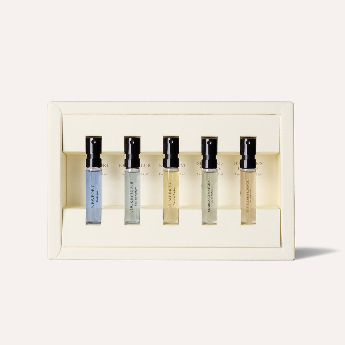 A cream-colored box holds the Caswell-Massey Fragrance Discovery Collection—six clear men’s spray bottles with black caps, neatly lined up in a row. The scene features a simple, light background.