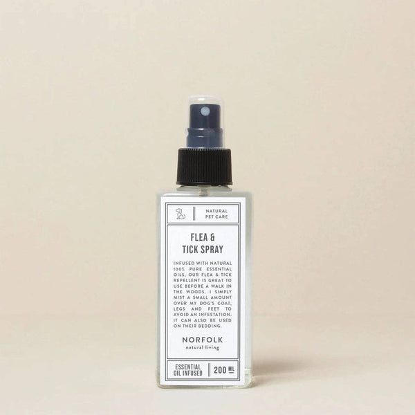 A clear spray bottle labeled "Norfolk Natural Living Flea & Tick Spray" stands upright against a light beige background. The 200 ml label notes it's a natural flea and tick repellent for dogs, infused with essential oils from Norfolk Natural Living.