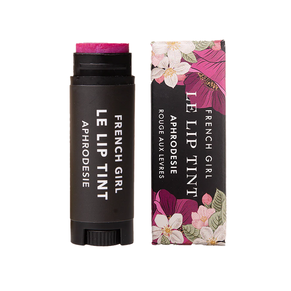 A tube and box of FRENCH GIRL Tinted Lip Balm in Aphrodesie. This hydrating balm comes in a black tube with white text, packaged in a box decorated with pink, white, and yellow floral designs.