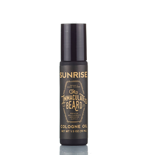 A black cylindrical bottle labeled "The Immaculate Beard SUNRISE Cologne Oil" with gold lettering, containing 10ml of woody fragrance cologne oil from The Immaculate Beard, stands upright on a white background.