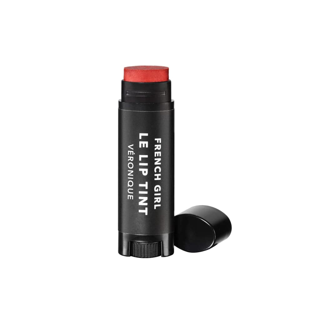 A black tube of FRENCH GIRL Tinted Lip Balm | Veronique with the cap off reveals its red tint. The product stands upright on a white background, showcasing the clean beauty values of FRENCH GIRL.