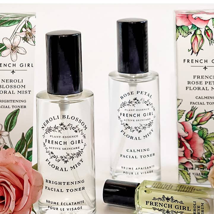 Two clear bottles of FRENCH GIRL Organic Floral Face Mist & Toner - Neroli Blossom with black caps stand upright amid floral packaging. A smaller green bottle labeled "FRENCH GIRL" highlights the organic skincare collection.