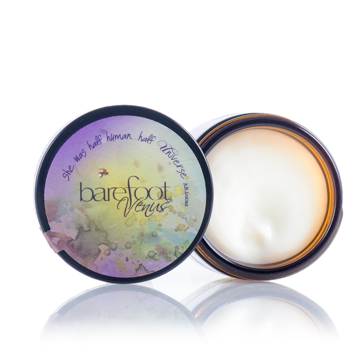 An open container of Barefoot Venus Lemon Freckle Hand Repair Balm with a colorful lid reading “She was half human...half universe.” The smooth, white shea butter-rich cream sits in the branded container on a white background.