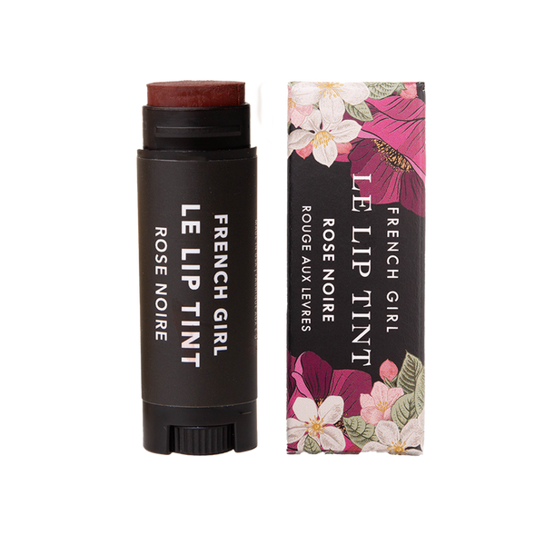 A black tube of FRENCH GIRL Tinted Lip Balm in Rose Noire is shown beside its box, which features a floral pattern with pink and white flowers and green leaves.