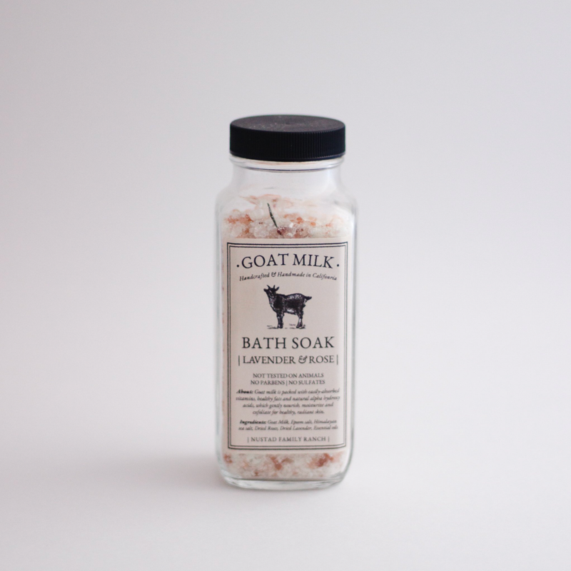 A jar of "Nustad Family Ranch Goat Milk Bath Soak" with lavender, rose petals, and epsom salts against a plain white background. The label features an illustration of a goat.