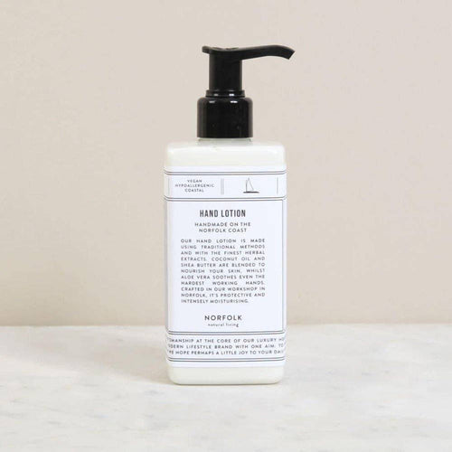 A white pump bottle of Norfolk Natural Living En Plein Air Natural Hand Lotion (300ml) with a minimalist label rests on a beige surface, described as handmade with natural extracts for optimal skin nourishment.