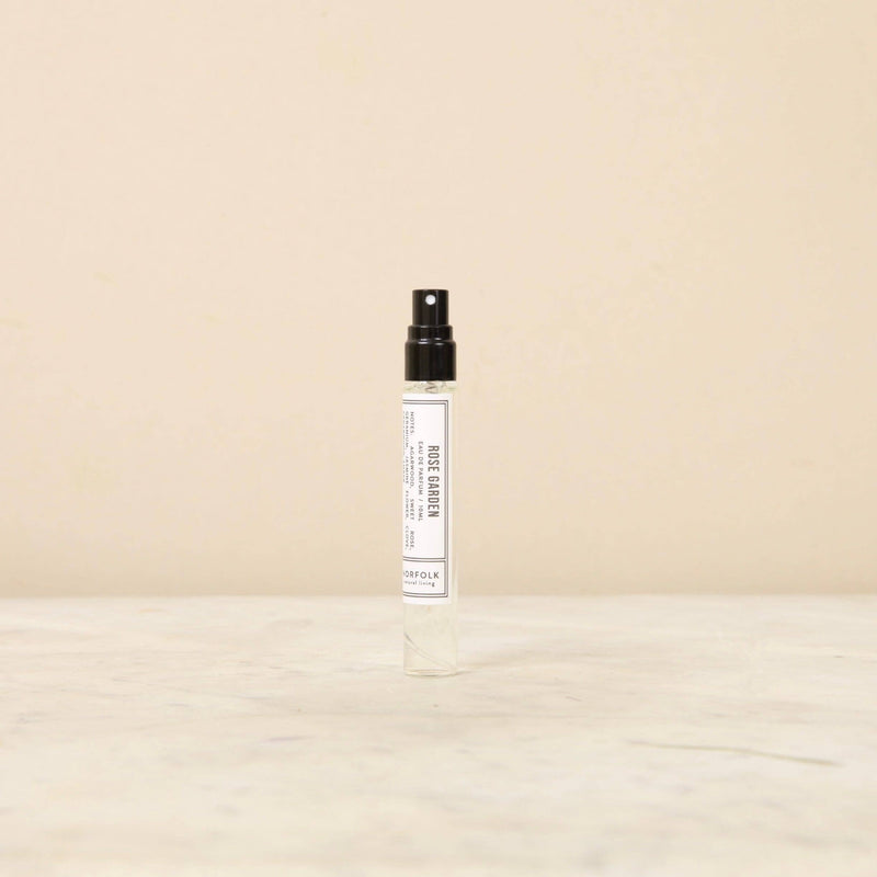 A Norfolk Natural Living Rose Garden Parfum 10ml with a black spray nozzle and a simple, white label stands on a beige surface against a matching background, containing long-lasting fragrance.