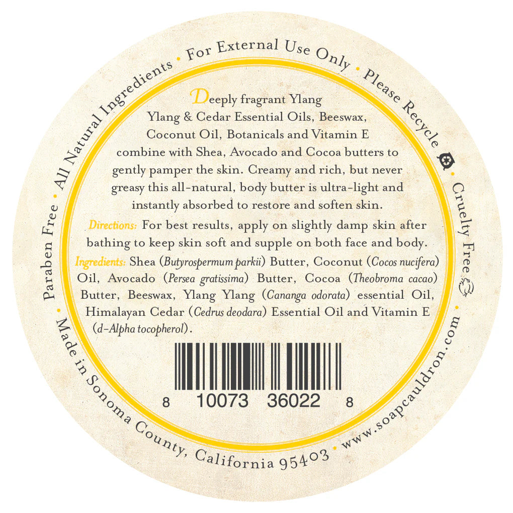 The Three Sisters Apothecary Ylang-Ylang Body Butter features a round label listing shea, coconut oil, avocado, beeswax, and botanicals. Directions appear in gold and black text on a cream background—ideal for this hydrating balm.