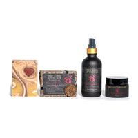 A display of Three Sisters Apothecary products. From left to right: a marbled soap bar with a heart design, infused with Rosewood; a rectangular soap bar in a decorated box; a coin-like item; a black spray bottle featuring the Heart of Darkness blend; and Three Sisters Apothecary Intentions Body Butter - Heart of Darkness in a small black jar—all labeled with the Three Sisters Apothecary logo.