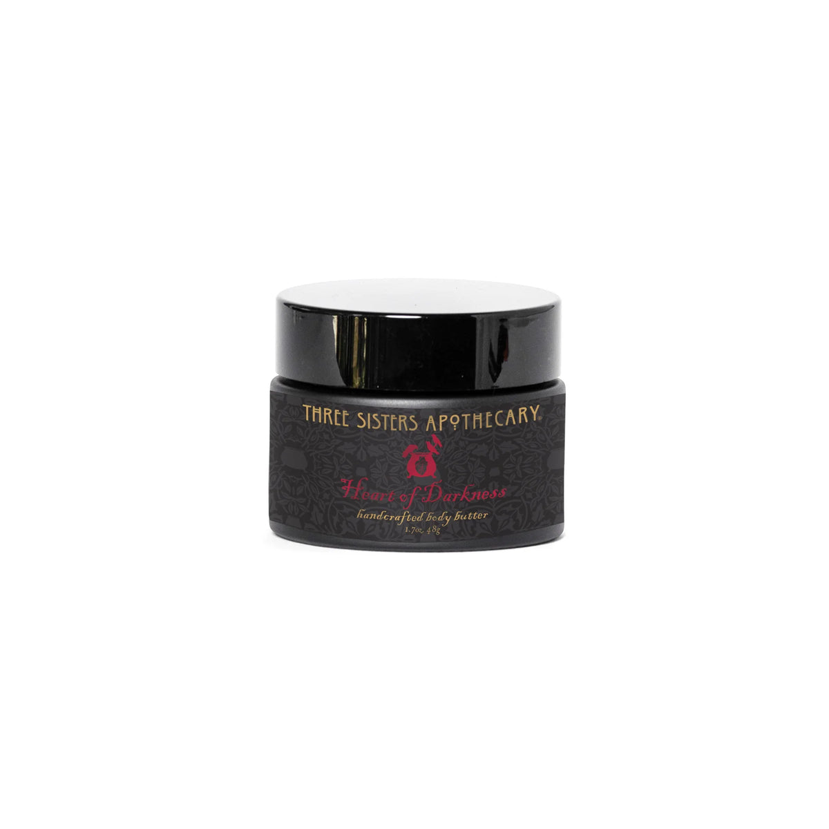 A small black jar with a black lid, labeled "Three Sisters Apothecary Intentions Body Butter - Heart of Darkness" in white, red, and gold text. The label includes elegant designs, a small decorative emblem, and notes of sandalwood in the Heart of Darkness blend.