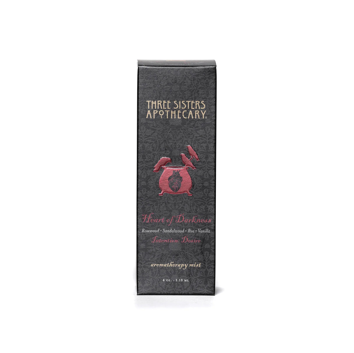 A gray box with intricate patterns, labeled "Three Sisters Apothecary," displays the product name "Intentions Aromatherapy Mist - Heart of Darkness" in red text. It highlights compassionate essential oils like Rosewood, Sandalwood, and Bourbon Vanilla. This 4 oz aromatherapy mist is a Heart of Darkness blend promoting love.