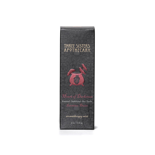 A gray box with intricate patterns, labeled "Three Sisters Apothecary," displays the product name "Intentions Aromatherapy Mist - Heart of Darkness" in red text. It highlights compassionate essential oils like Rosewood, Sandalwood, and Bourbon Vanilla. This 4 oz aromatherapy mist is a Heart of Darkness blend promoting love.