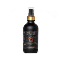 A black spray bottle adorned with a gold collar and a pump top. The label reads "Three Sisters Apothecary - Intentions Aromatherapy Mist - Manifestation Magic." Infused with essential oils, the design showcases a mystical theme with intricate patterns and a central emblem resembling an alchemical symbol.