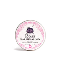 A round tin container labeled "Three Sisters Apothecary Soothing Rose & Marshmallow Salve with Arnica, 2.5 oz, 71 g." The design features intricate pink floral patterns around the edges and a dark blue logo at the top center, highlighting its nourishing skin salve enriched with rose absolute.