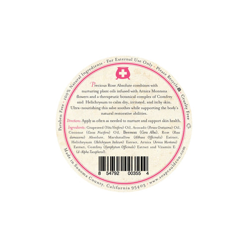The product label for Three Sisters Apothecary Soothing Rose & Marshmallow Salve with Arnica features a round, white design with a pink band at the center and a prominent white medical cross symbol. The label highlights the nourishing ingredients, including Rose Absolute, Arnica Montana, and Comfrey. It is recommended for dry, irritated, and itchy skin, specifically noting its 100% natural ingredients known for their restorative properties.