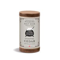 Three Sisters Apothecary Therapeutic Foaming Coastal Cedar (20oz) features menthol and arnica to help relieve muscle tension. The cylindrical container has a gray label with decorative borders and a small cauldron illustration.
