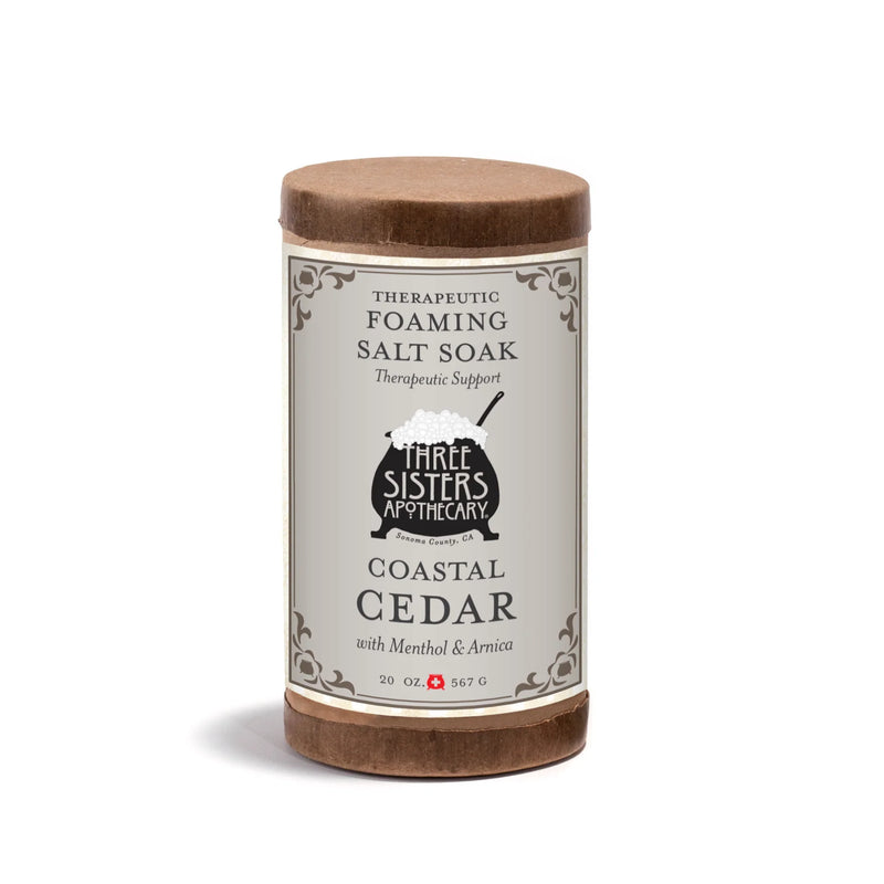 Three Sisters Apothecary Therapeutic Foaming Coastal Cedar (20oz) features menthol and arnica to help relieve muscle tension. The cylindrical container has a gray label with decorative borders and a small cauldron illustration.