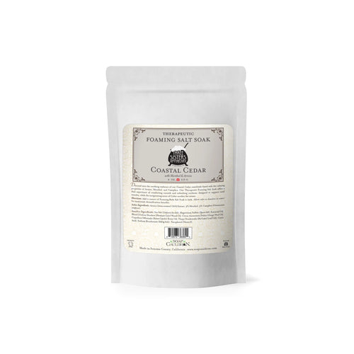 A white stand-up pouch of Three Sisters Apothecary Therapeutic Foaming Coastal Cedar 20oz, featuring black text on a beige label, offers detoxifying bath salts for muscle tension relief, set against a plain white background.
