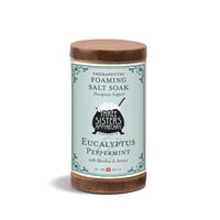 A 20oz cylindrical container of Three Sisters Apothecary Therapeutic Foaming Eucalyptus & Peppermint, featuring Epsom salts and a blue and brown label with decorative borders.