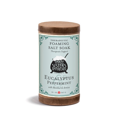 A 20oz cylindrical container of Three Sisters Apothecary Therapeutic Foaming Eucalyptus & Peppermint, featuring Epsom salts and a blue and brown label with decorative borders.