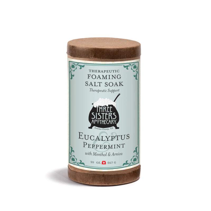 A 20oz cylindrical container of Three Sisters Apothecary Therapeutic Foaming Eucalyptus & Peppermint, featuring Epsom salts and a blue and brown label with decorative borders.