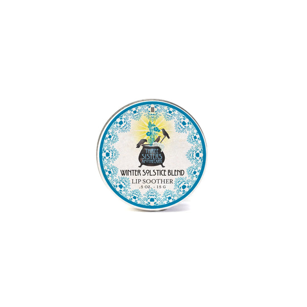 A round tin of Three Sisters Apothecary Winter Solstice Lip Soother by Three Sisters Aphothecary, featuring essential oils for natural lip care, a blue border, and a central raven logo with a winter design.