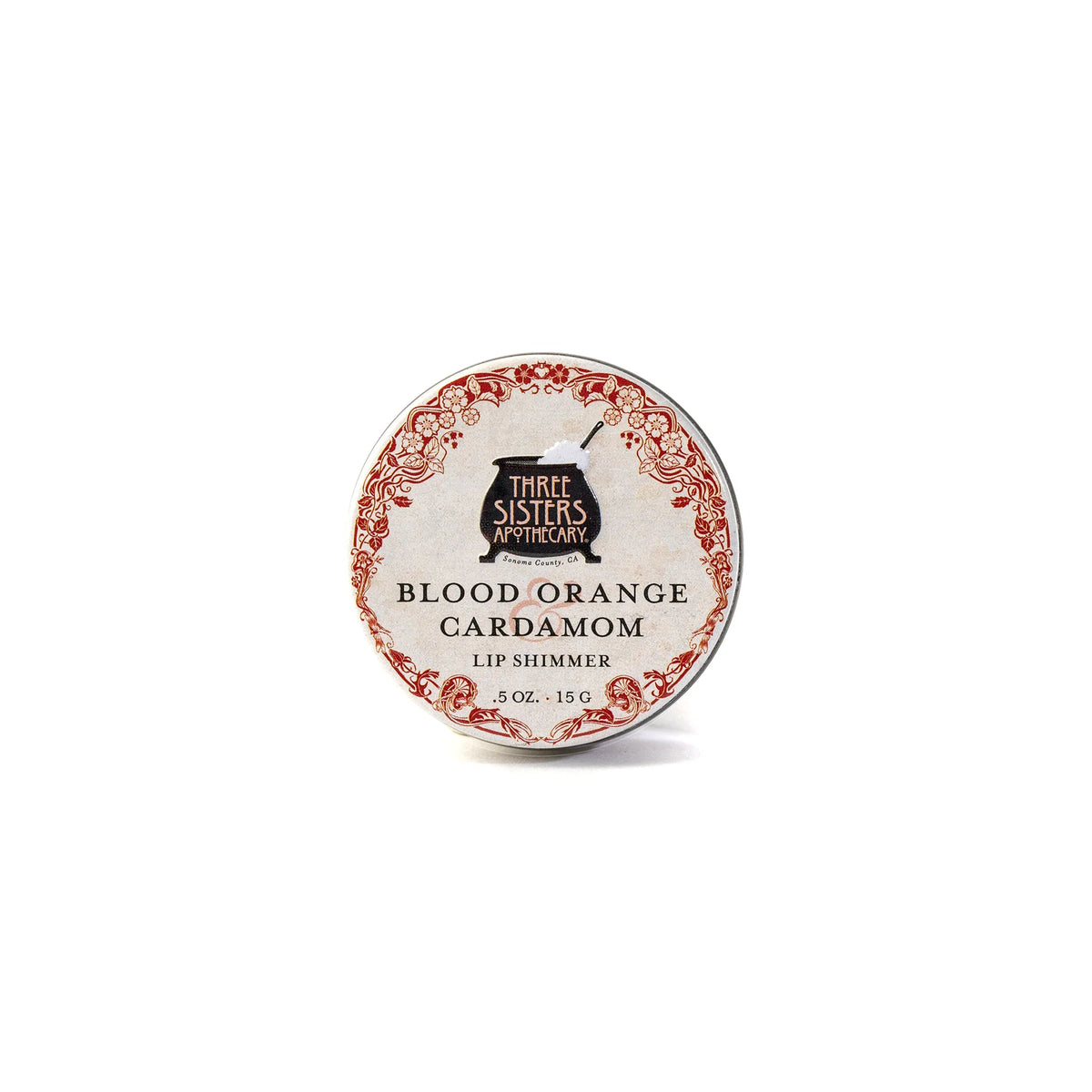 A round tin of hydrating Three Sisters Apothecary Blood Orange & Cardamon Lip Shimmer, made with natural beeswax, has a vintage-style red and white label with black text.