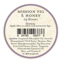 A round label for Three Sisters Apothecary California Mission Fig & Honey Lip Shimmer has directions to apply often for soft, hydrated lips, a barcode, and ingredients such as beeswax, oils, butters, honey, fig, tangerine oil, mica, and vitamin E.