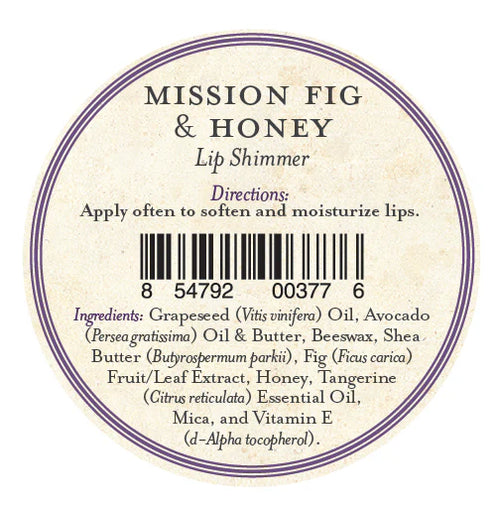 A round label for Three Sisters Apothecary California Mission Fig & Honey Lip Shimmer has directions to apply often for soft, hydrated lips, a barcode, and ingredients such as beeswax, oils, butters, honey, fig, tangerine oil, mica, and vitamin E.