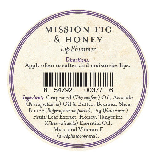 A round label for Three Sisters Apothecary California Mission Fig & Honey Lip Shimmer has directions to apply often for soft, hydrated lips, a barcode, and ingredients such as beeswax, oils, butters, honey, fig, tangerine oil, mica, and vitamin E.