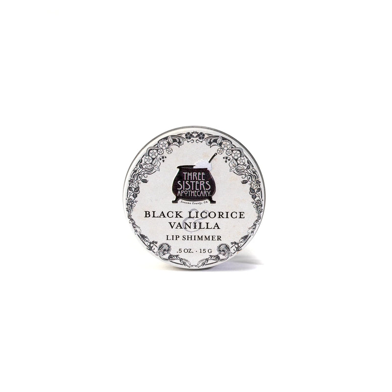 A round tin labeled "Three Sisters Aphothecary Black Licorice & Vanilla Lip Soother, 0.5 oz, 15 g" features floral designs on white. This hydrating balm is made with natural beeswax for soothing care.
